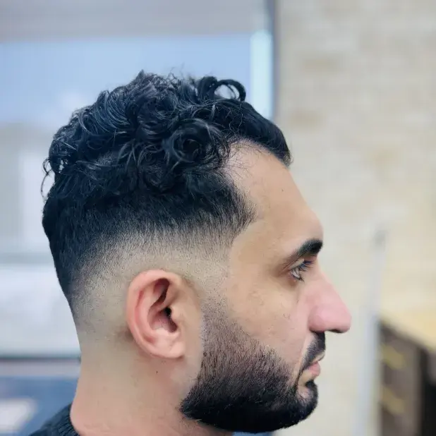 Curly top with a low skin fade and a short boxed beard